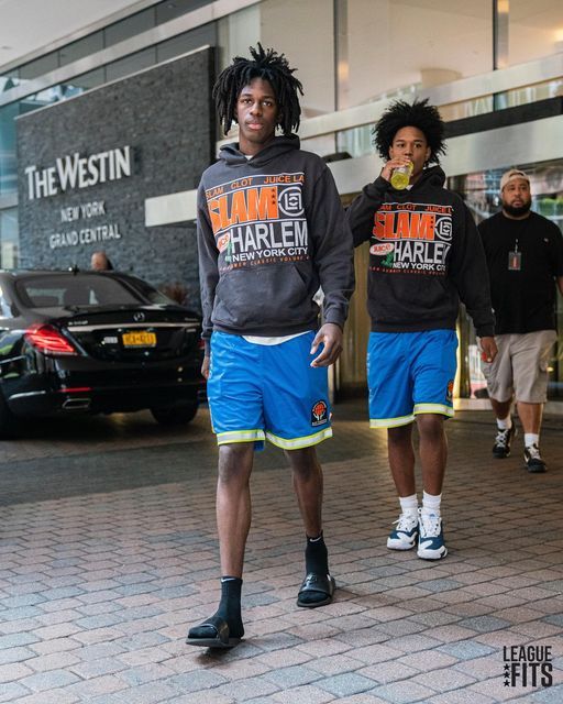 two young men are walking down the street wearing matching sweatshirts with shorts and sneakers