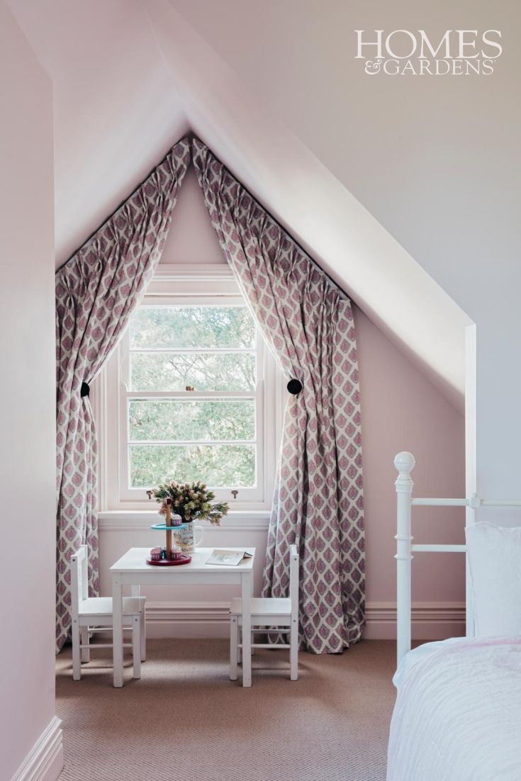 a bedroom with pink walls and curtains on the window sill, white table and chairs