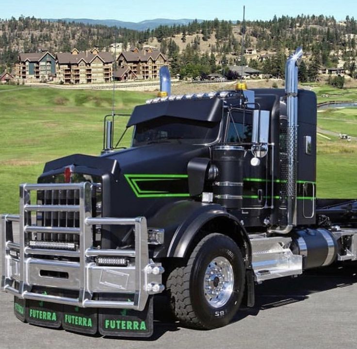 a large semi truck parked in a parking lot next to a green field and houses