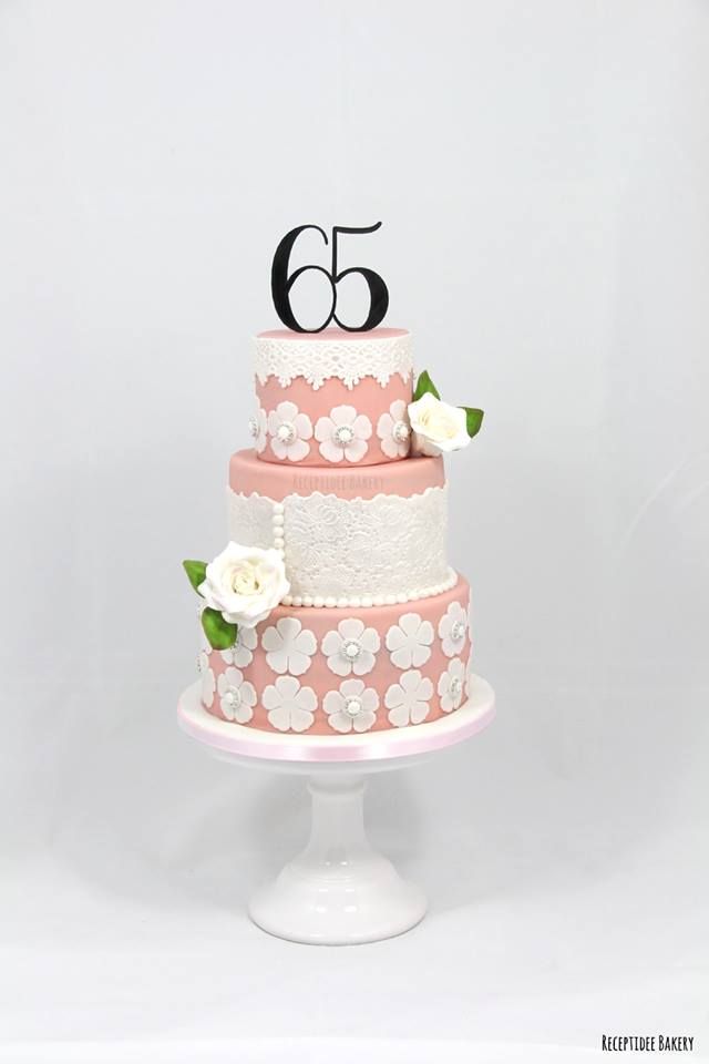 a pink and white wedding cake with flowers on the bottom tier is decorated with black number 65