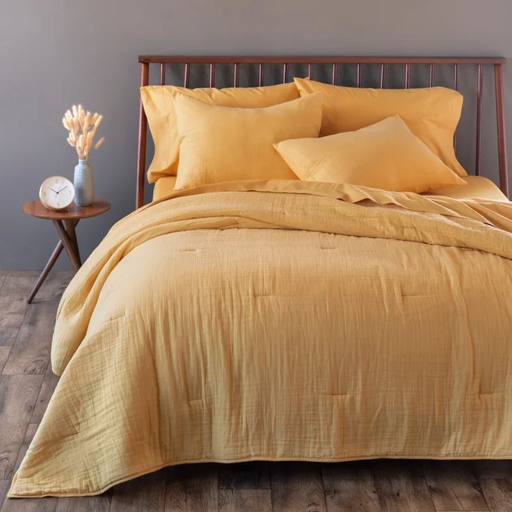 a bed with yellow sheets and pillows on top of it next to a night stand