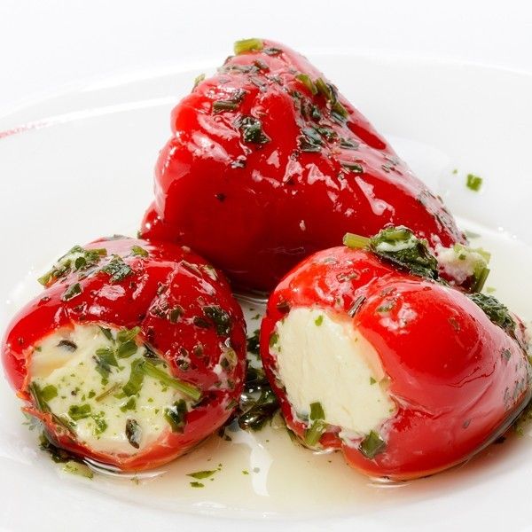 three stuffed tomatoes on a white plate covered in cheese and herbs, ready to be eaten