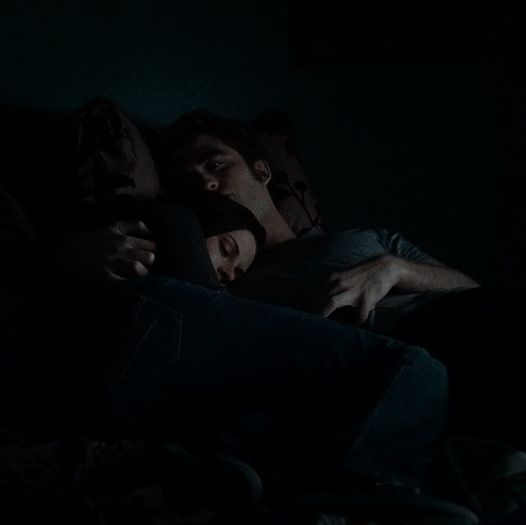 two people sleeping in the dark with their heads on each other's shoulders,