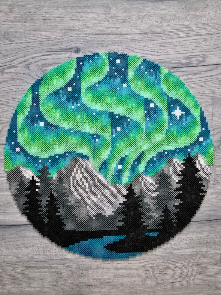 a cross stitch pattern with an image of the northern lights in the sky and mountains