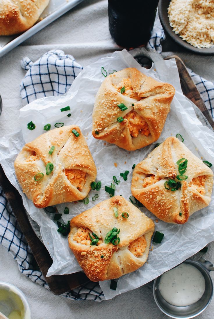 four pieces of bread with cheese and green onions on top, sitting on a piece of parchment paper