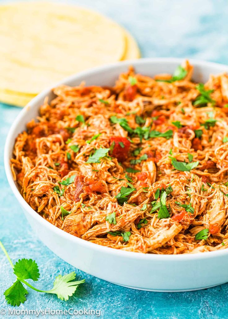 a white bowl filled with shredded chicken and garnished with cilantro