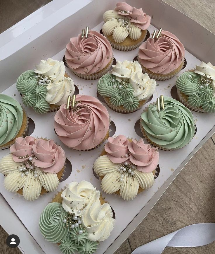 a box filled with lots of cupcakes on top of a wooden table next to a white ribbon