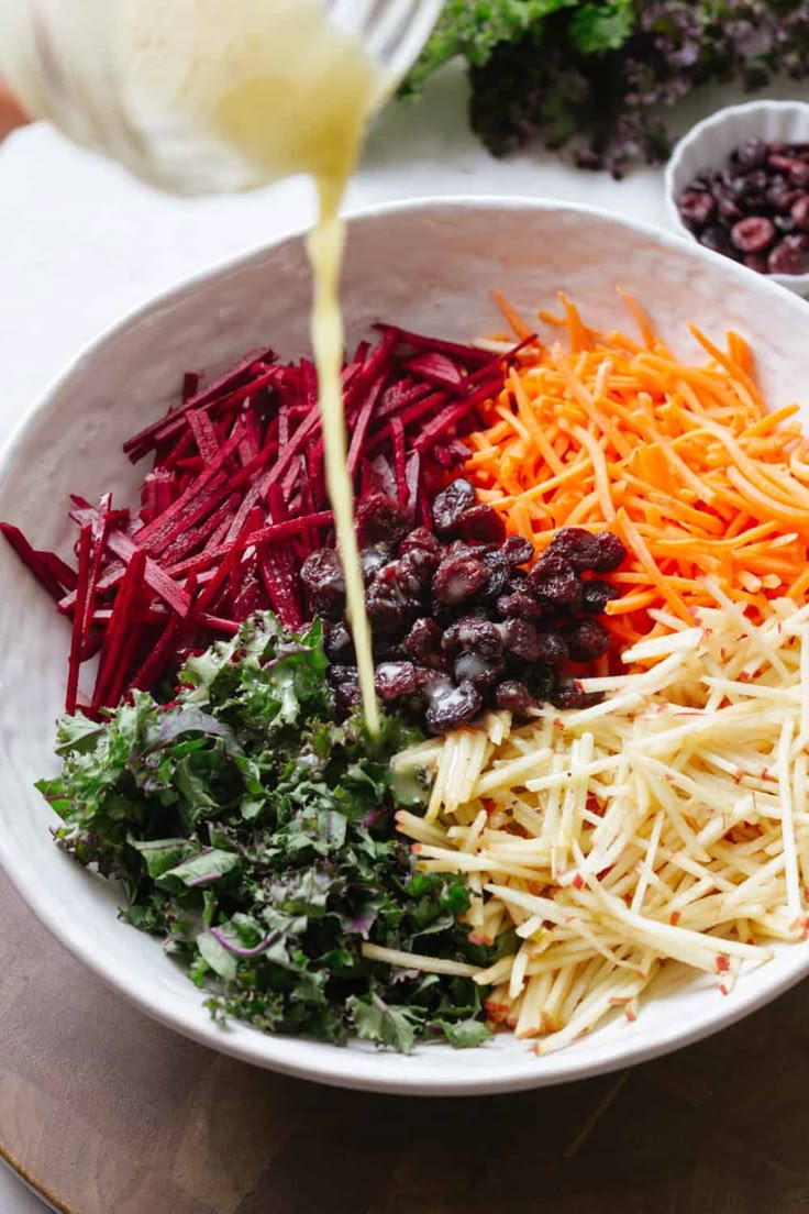 someone pouring dressing into a white bowl filled with different types of vegetables and cheeses