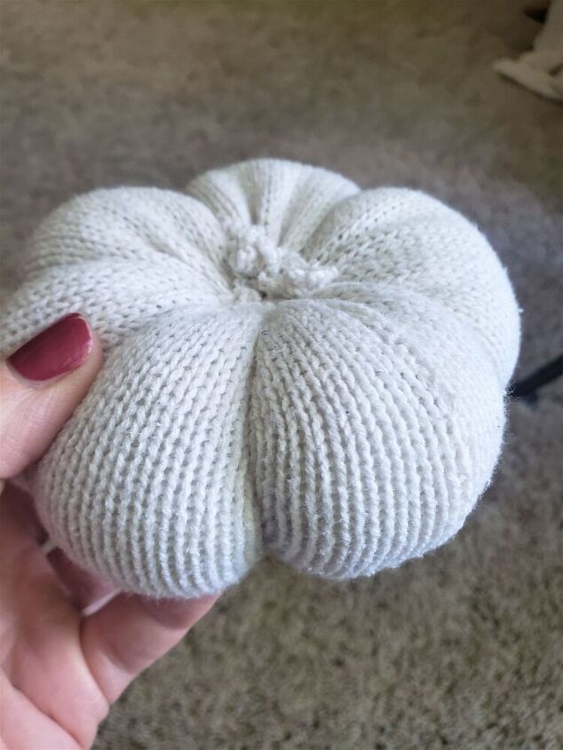 a hand holding a white knitted object in it's left hand on the floor