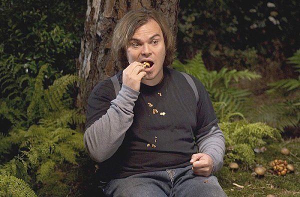 a man sitting on the ground eating something with his mouth wide open in front of a tree