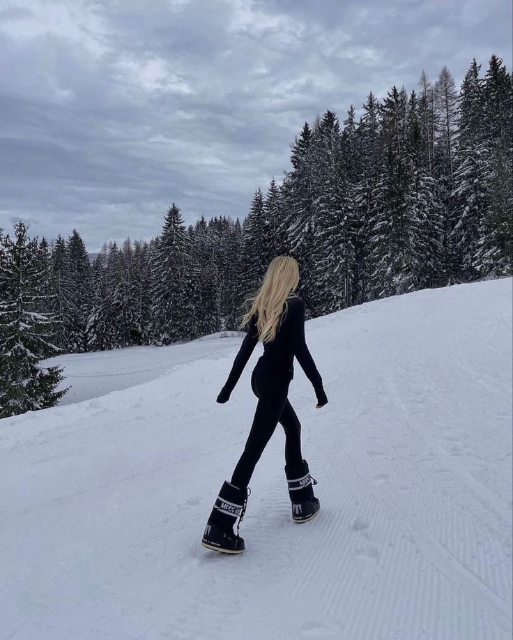 a woman is snowboarding down a hill in the winter with pine trees behind her