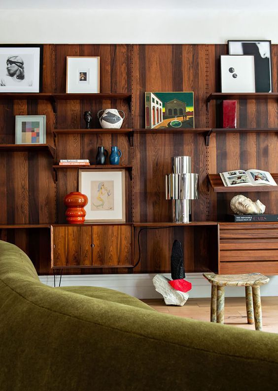 a living room filled with furniture and bookshelves next to a green couch in front of a wooden wall