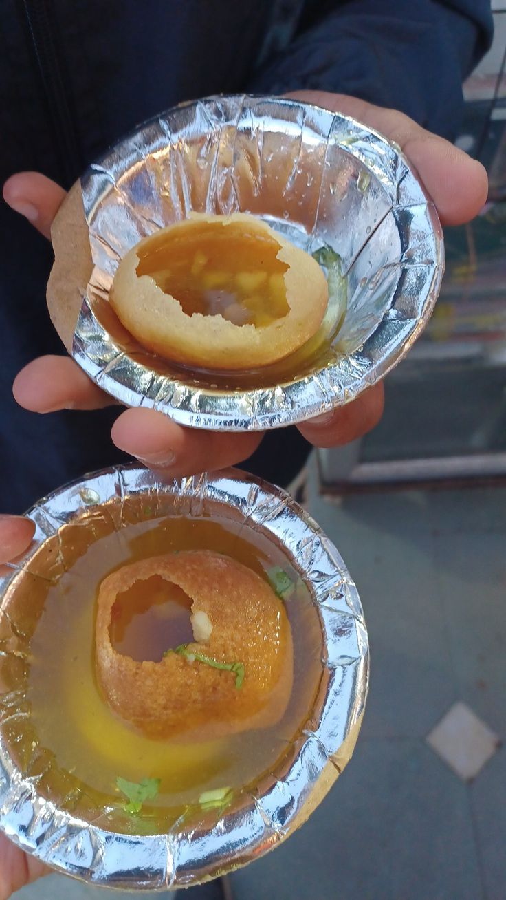 two silver foil plates with some food inside of them on top of each other in their hands