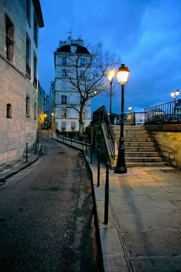 an empty street at dusk with stairs leading up to the building on the right side