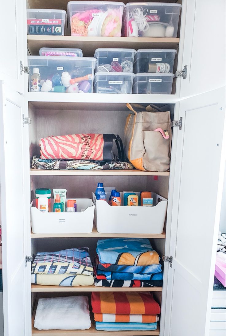 an organized closet with clear bins and plastic containers on the bottom shelf for storage