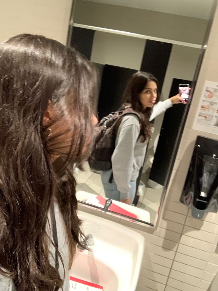 a woman taking a selfie in front of a mirror with her hair blowing back