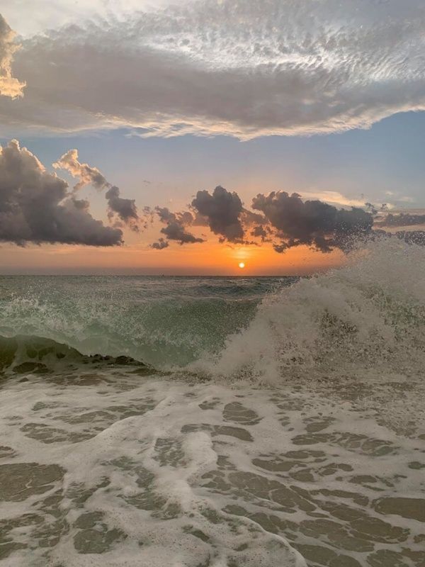 the sun is setting over the ocean with waves crashing in front of it and some clouds