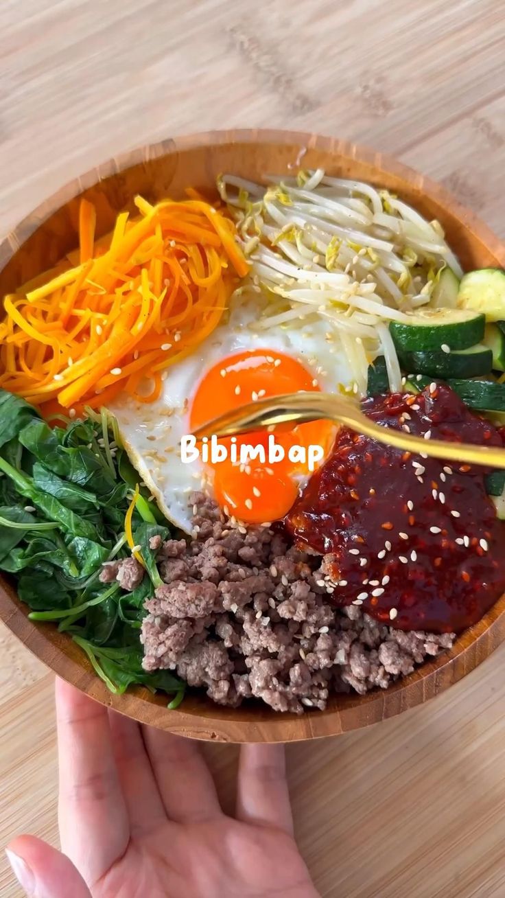 a person holding a wooden bowl filled with different types of vegetables and meats on top of it