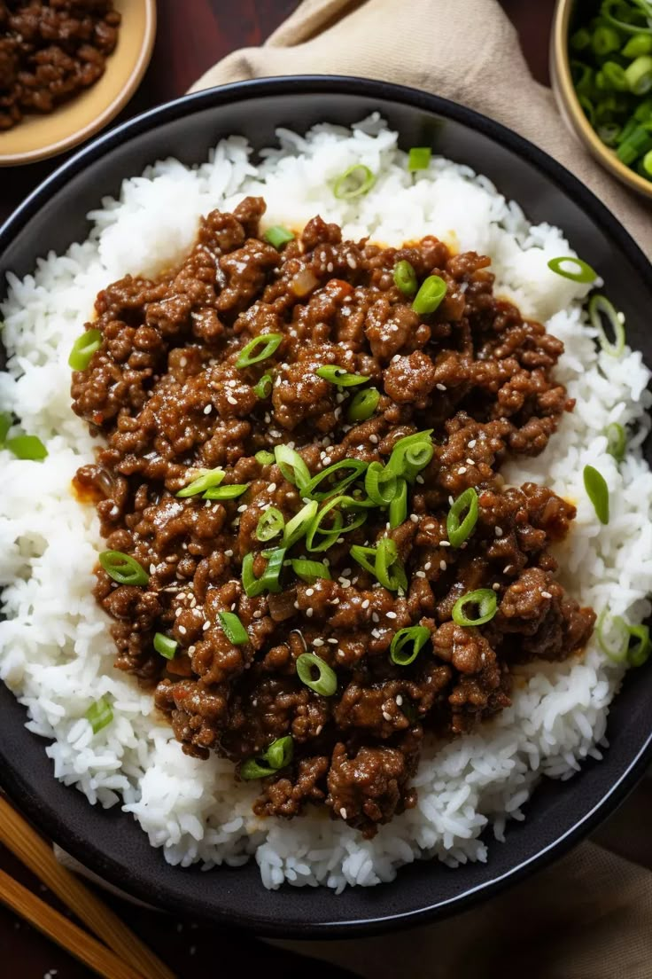 a black plate topped with rice and ground beef next to bowls of green onions, peas and chopsticks