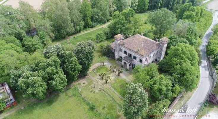 an old house in the middle of some trees and grass with a river running through it