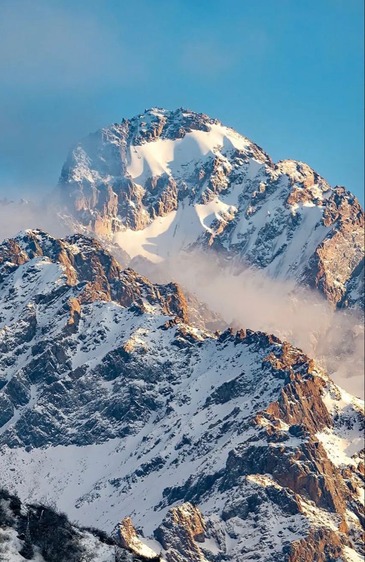 the top of a snow covered mountain with clouds in the foreground and blue sky above