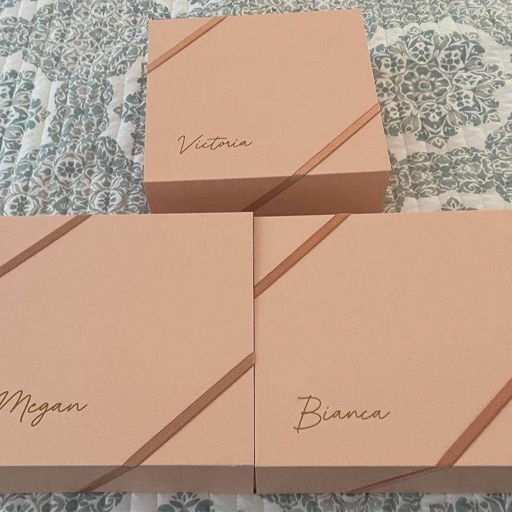 three pink boxes sitting on top of a bed next to each other with writing on them