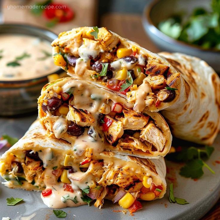 two burritos stacked on top of each other with sauce and vegetables in the background