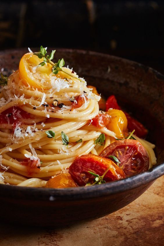 pasta with tomatoes, parmesan cheese and herbs in a brown bowl on a wooden table