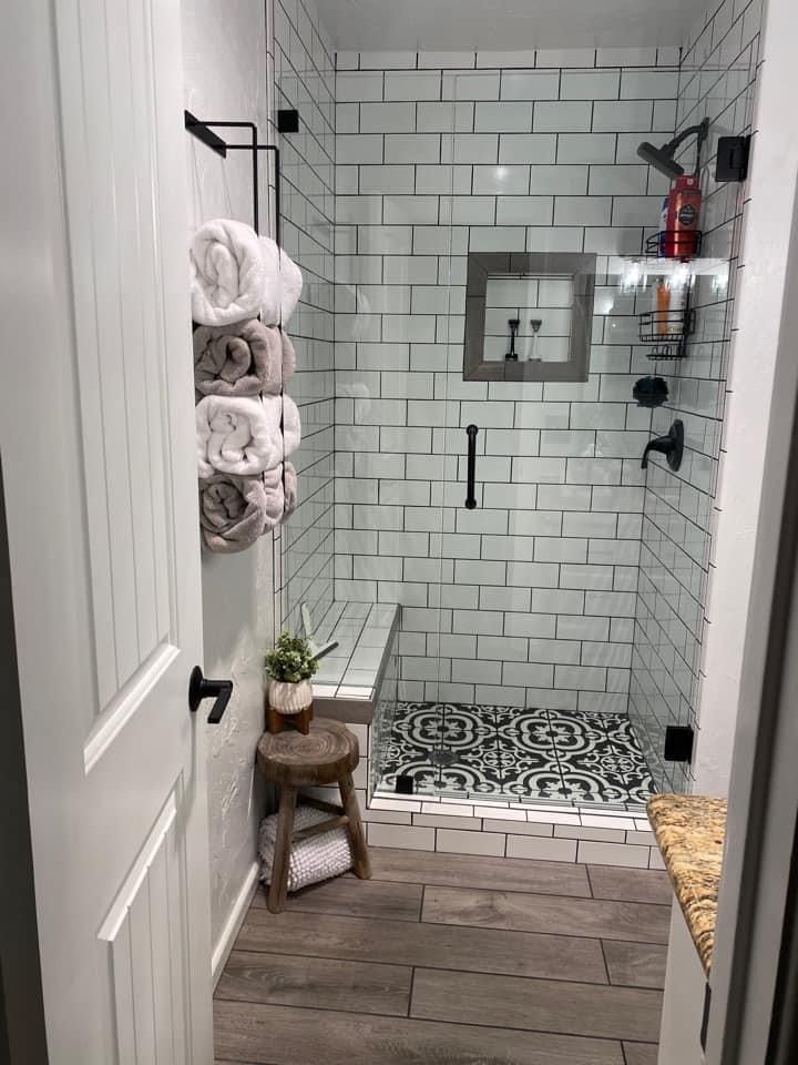 a walk in shower sitting next to a wooden stool and white walls with black accents