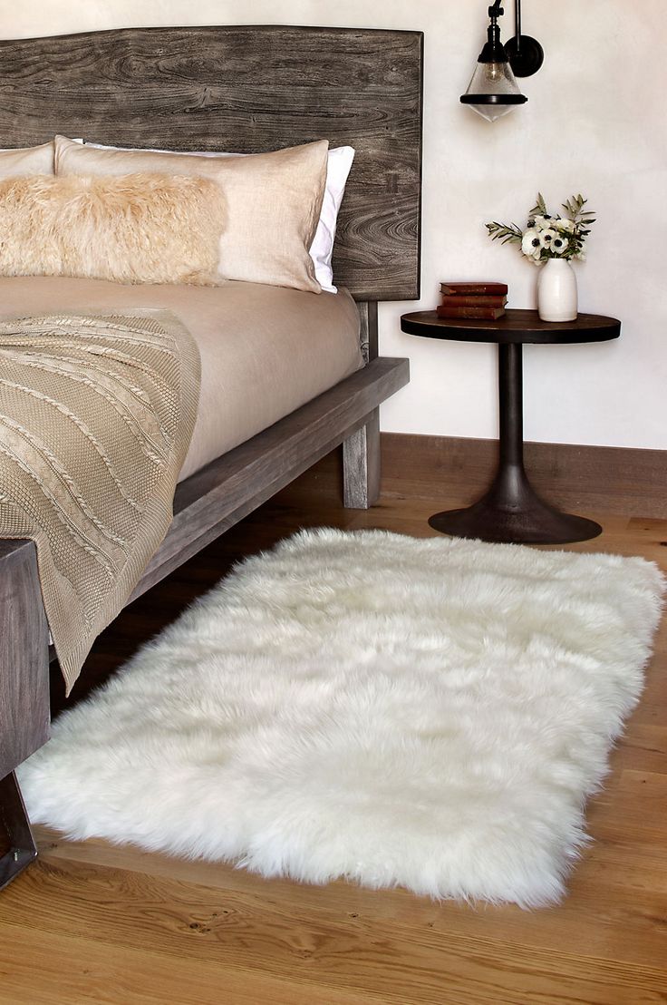 a bedroom with a bed, night stand and white fur rug on the wooden floor