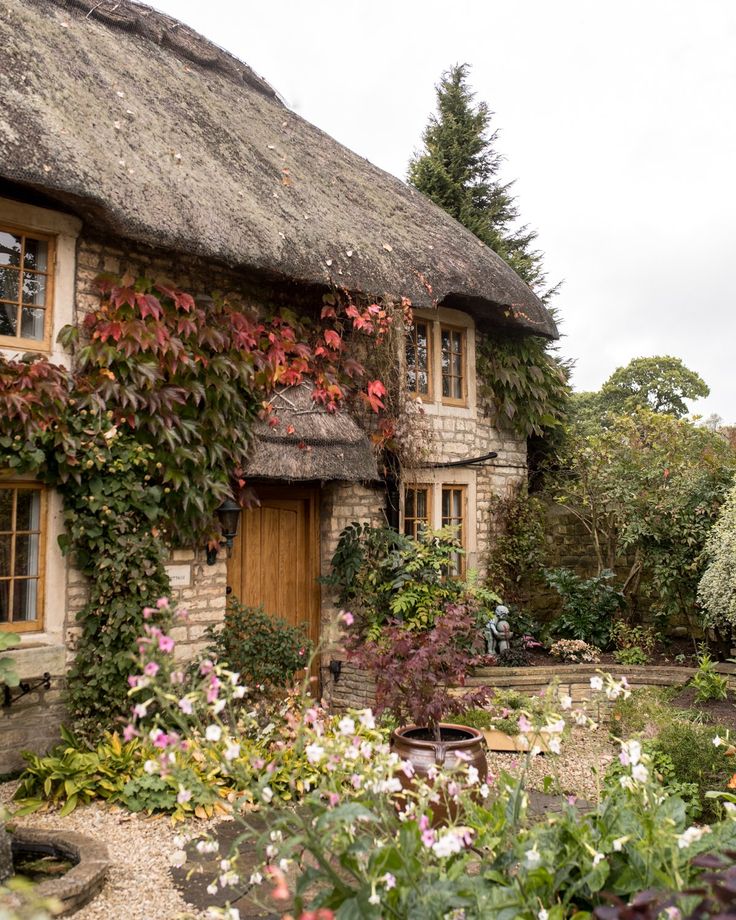 a thatched roof house with flowers and trees around it