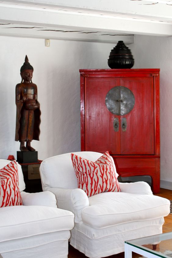 a living room with white furniture and red accents