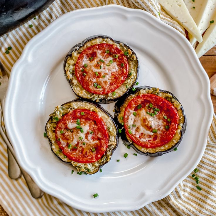 three stuffed eggplant halves on a white plate with cheese and parmesan