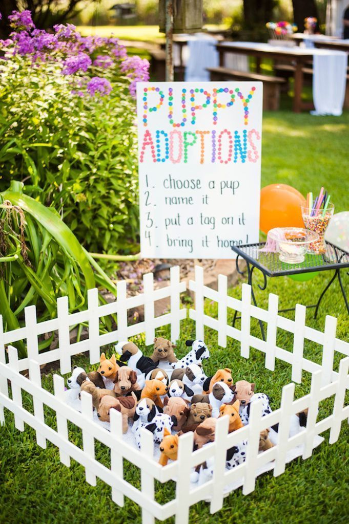 a white picket fence with stuffed animals in it and a sign that says puppy adoption station from a puppies and sprinkles birthday party on kora's party