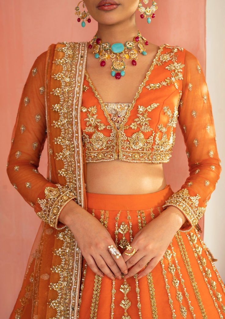 Orange Color Lehenga Choli for Pakistani Mehndi Wear is Embellished with a work of the finest multiple color embroidery, the Orange Lehenga Dupatta comes with three-quartered sleeves and a stylish round neckline. This graceful bridal wear is made with pure organza and styled with floral motifs. The orange blouse choli follows a stunning orange lehenga, while an orange net dupatta makes the dress ready to have you admired on your Mehndi. Lehenga Choli: A citrus bridal tale, crafted passionately u Orange Chikankari Lehenga, Orange Net Blouse Designs, Orange Colour Bridal Lehenga, Orange Lehnga Design, Orange Colour Dress Design, Rust Colour Lehenga, Traditional Kundan Wear With Long Sleeves For Festivals, Bollywood Orange Anarkali Set With Intricate Embroidery, Orange Colour Blouse Designs