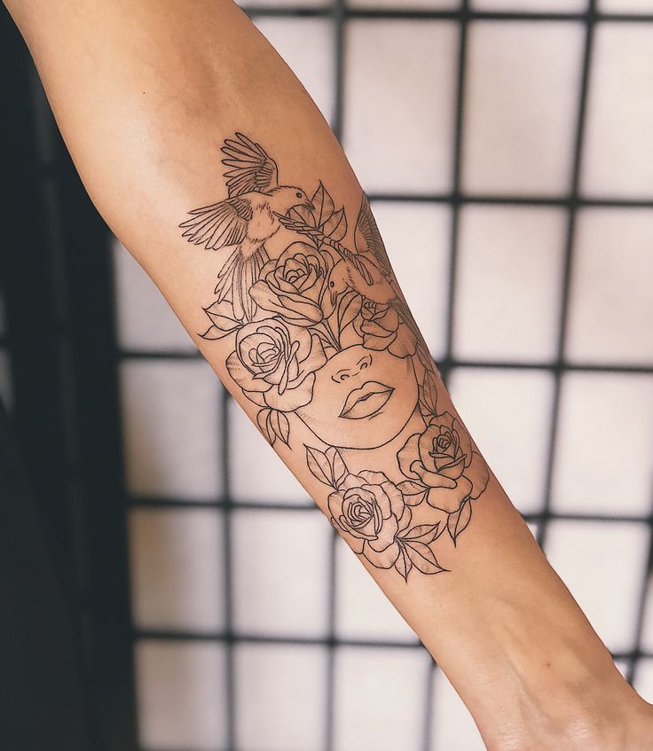 a woman's arm with flowers and a bird tattoo on her left arm, next to a tiled wall