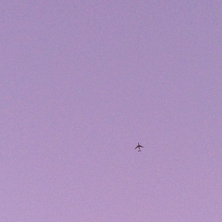 an airplane is flying high in the sky at dusk or dawn, with no clouds