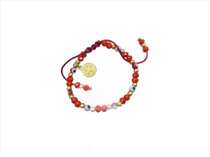 a bracelet with red beads and a gold coin on it, sitting on a white surface