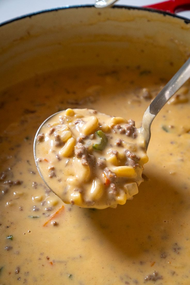 a ladle full of macaroni and cheese soup with a spoon in it