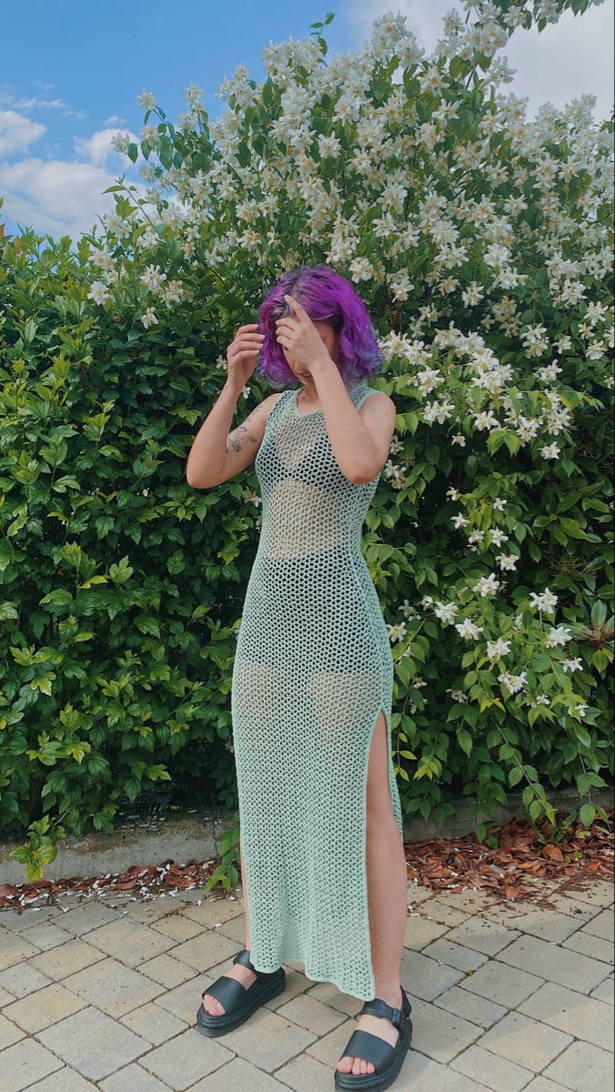 a woman with purple hair standing in front of bushes