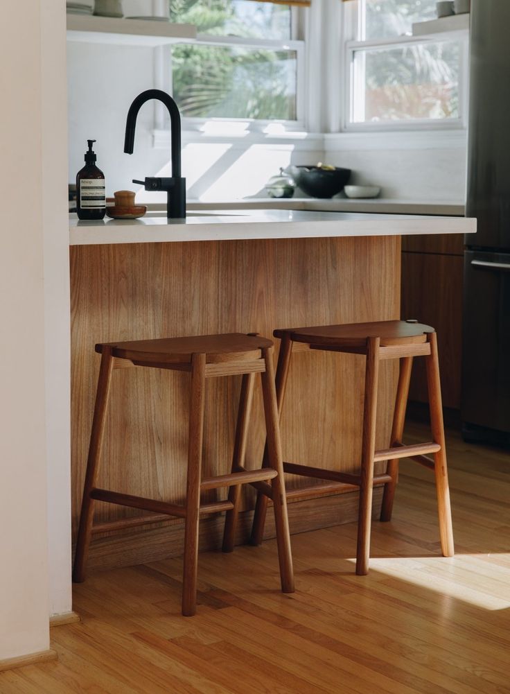 two wooden stools sit in front of the kitchen counter