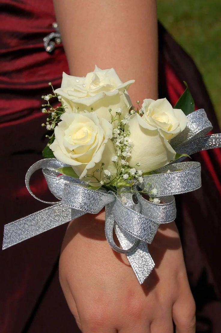 a bouquet of white roses tied to a silver ribbon on someones arm in a red dress