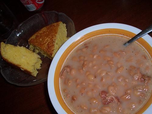 a bowl of beans and cornbreads next to a plate with a piece of bread