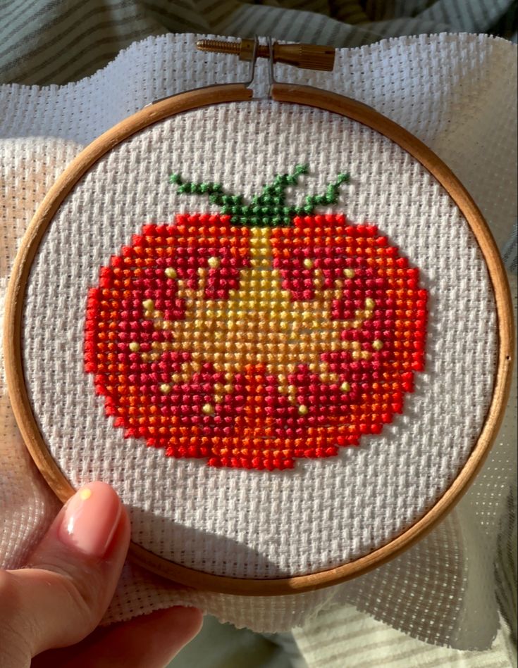 a hand holding a small cross stitched tomato