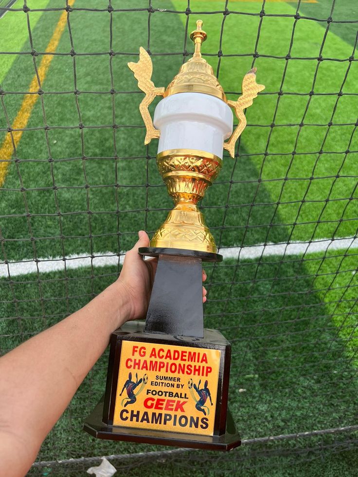 a person holding up a trophy in front of a soccer goal with the words e g academy championship written on it