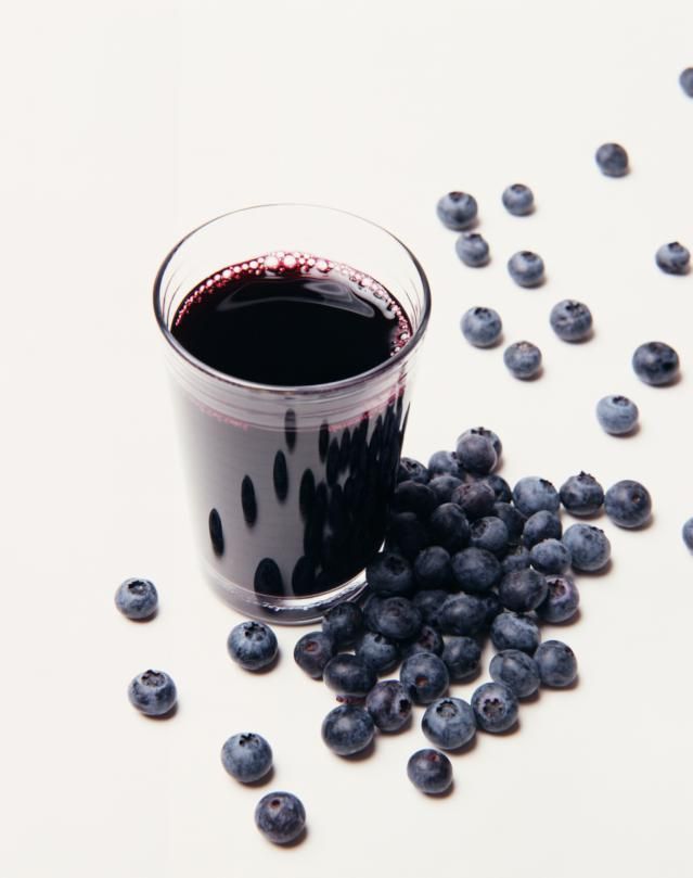 a glass filled with blueberries sitting on top of a white table next to berries