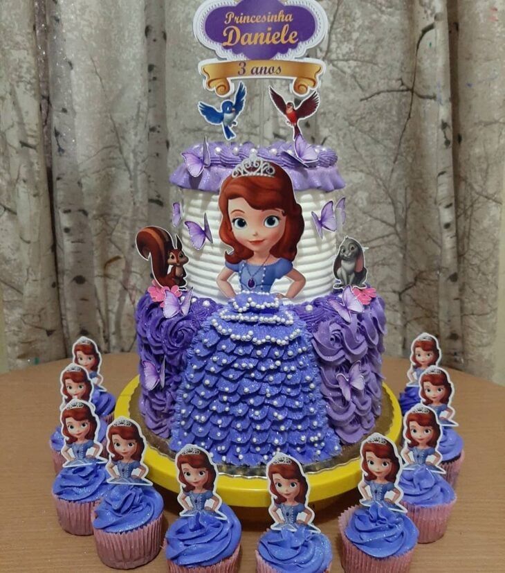 there is a cake with cupcakes on the table and pictures of princesses