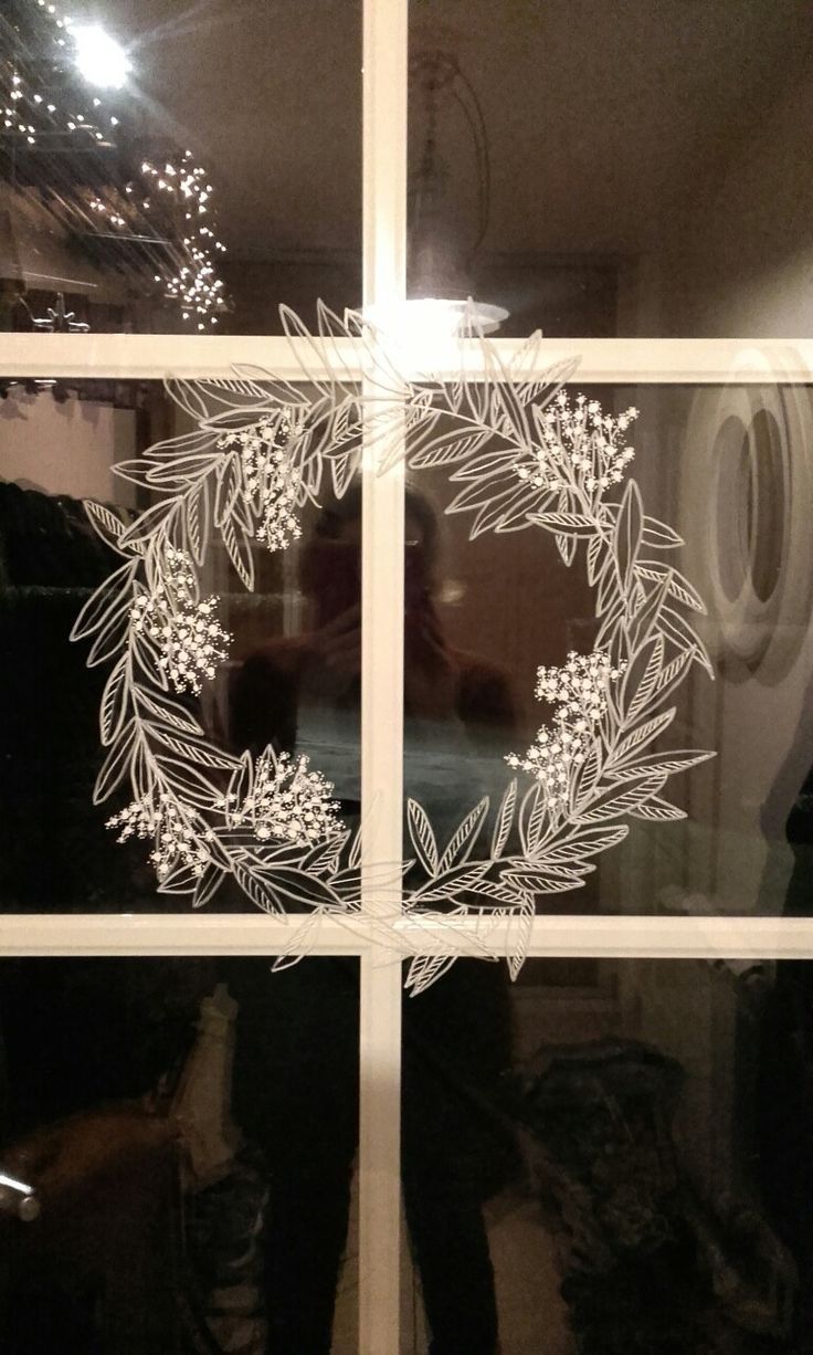 the reflection of a person standing in front of a window with a wreath drawn on it