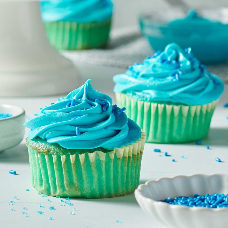 cupcakes with blue frosting and sprinkles on a white table