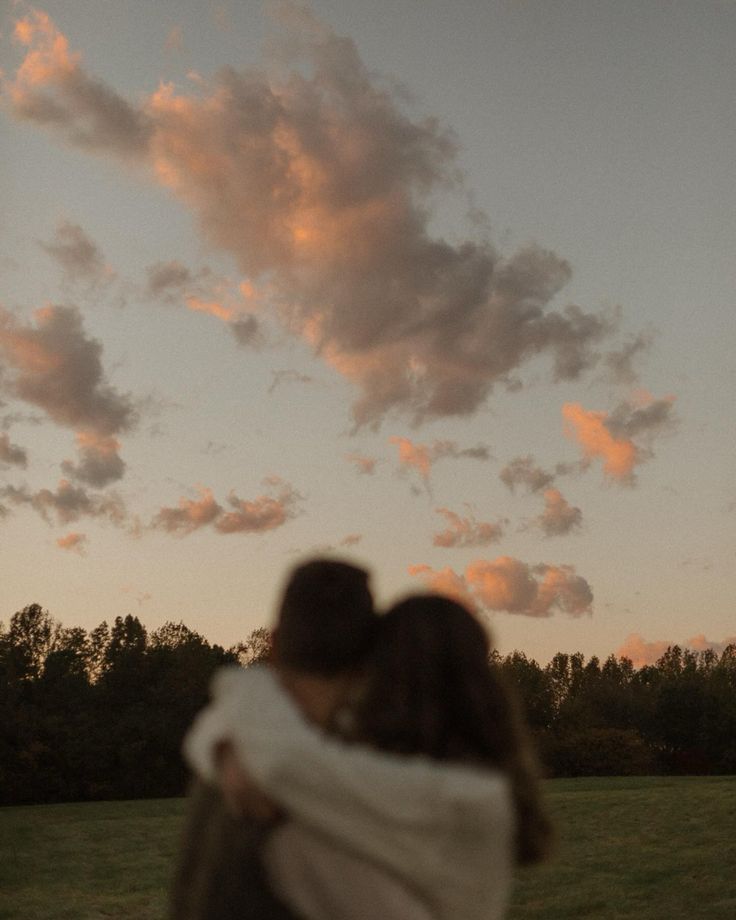 a man and woman embracing each other while the sun is setting in the sky behind them